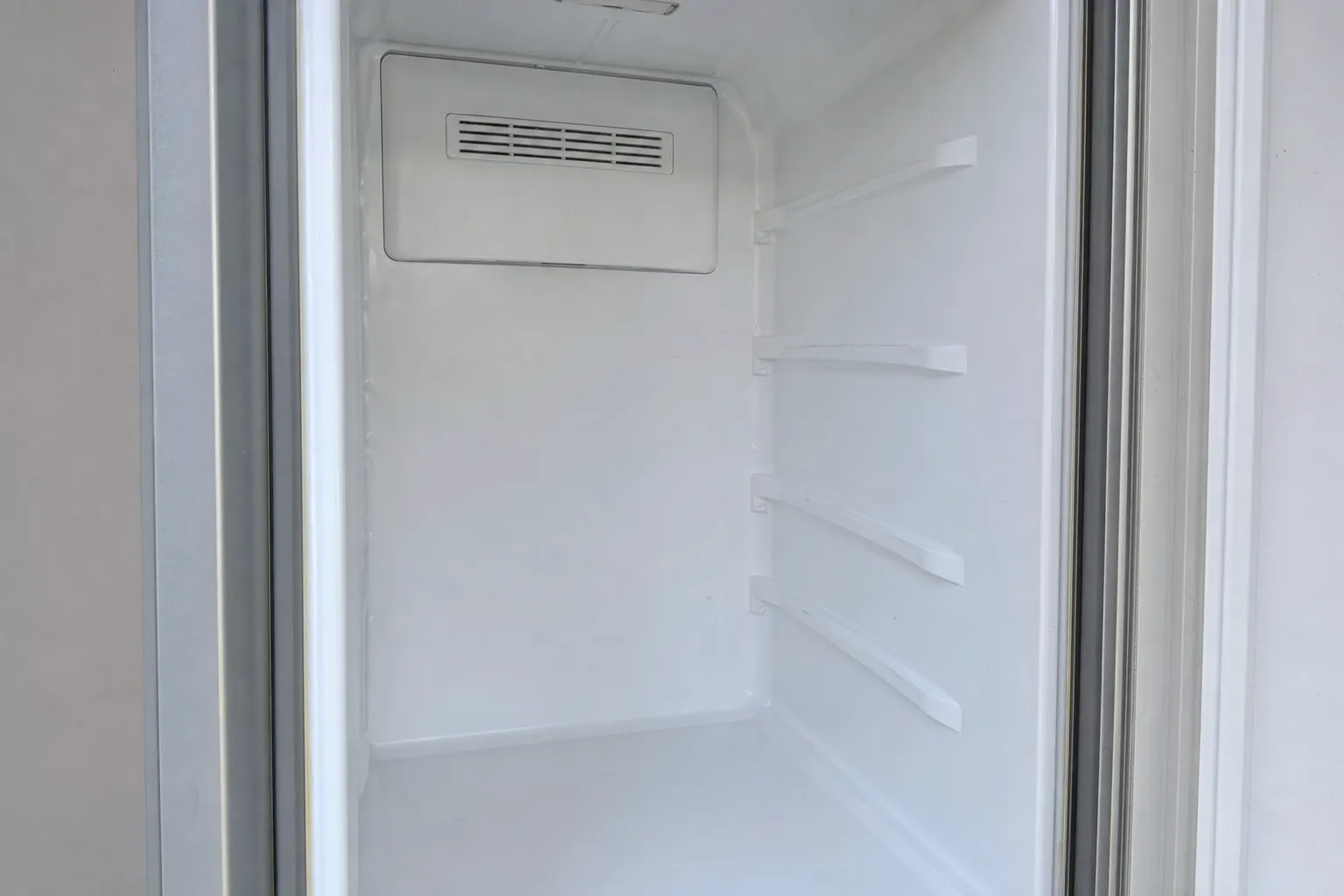 An empty white-lined compartment seen through its open door, a louvred duct cover at the top of the back wall